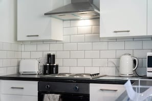 A modern kitchen with white cabinets, a gas stove, a kettle, and a coffee maker.
