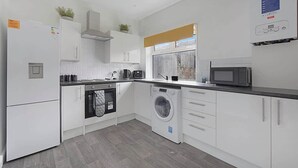 Een moderne keuken met witte kasten, een ingebouwde oven, een wasmachine en een magnetron.