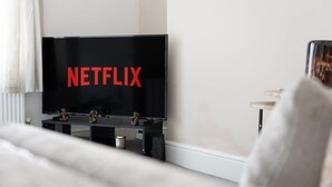 Een moderne woonkamer met een grote flatscreen-tv waarop 'NETFLIX' in rode letters staat, een bijzettafeltje met decoratieve objecten en een bank.
