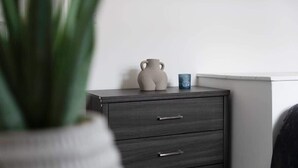 Een donker houten nachtkastje met twee lades en een keramieken vaas met handgrepen.