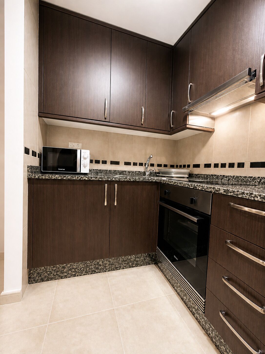 Una cocina con armarios de madera oscura, un microondas, un fregadero y un horno.