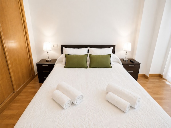 Una cama bien hecha con dos almohadas, dos mesitas de noche con lámparas y un armario de madera.
