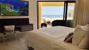 Una camera d'albergo con un letto, una TV a parete, una scrivania e vista sulla spiaggia dalla finestra.