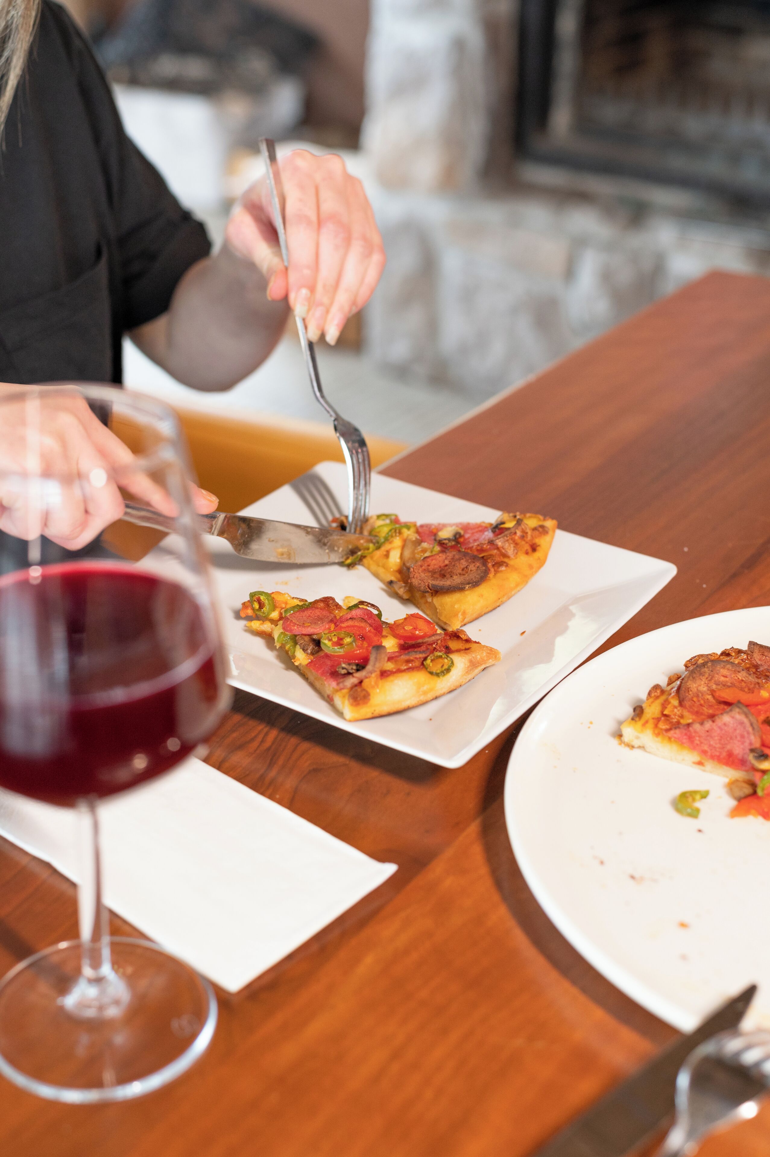 Una mesa con porciones de pizza, una copa de vino y cubiertos.
