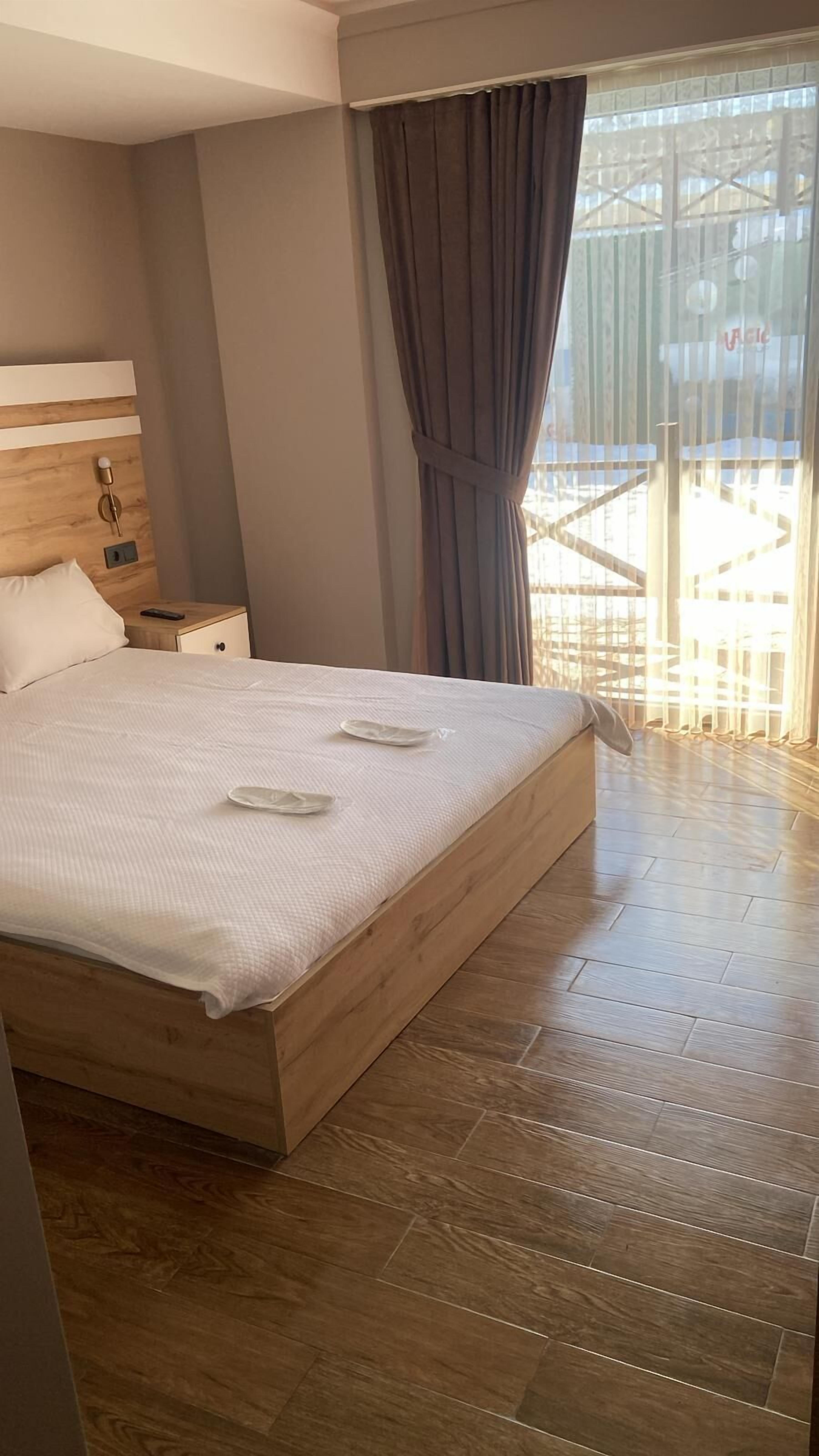 A bedroom with a large bed, wooden headboard, bedside table, and a view of a balcony with a railing.