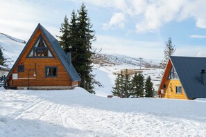 Two wooden cabins with pitched roofs, surrounded by snow and trees, set against a mountainous backdrop. - ÇAMBAŞI KAYAK VE DOĞA TESİSİ (Kabadüz)