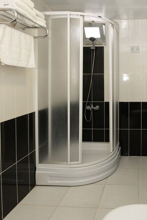 A shower enclosure with a control panel, a towel rack with folded towels, and black and white tiled walls.