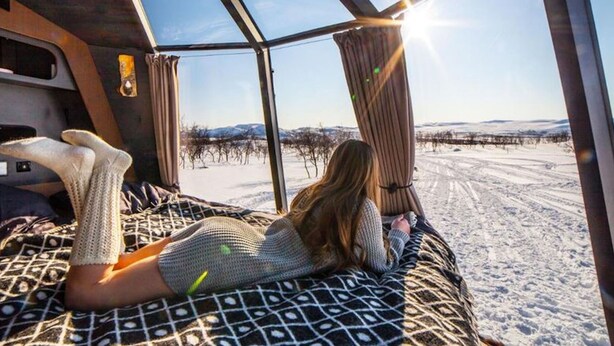 A person lying on a bed with a patterned bedspread, looking out of a window at a snowy landscape. - "suite With Lake View for 2 Guests Peace & Quiet Hotel in Jokkmokk Sweden" (Jokkmokk)