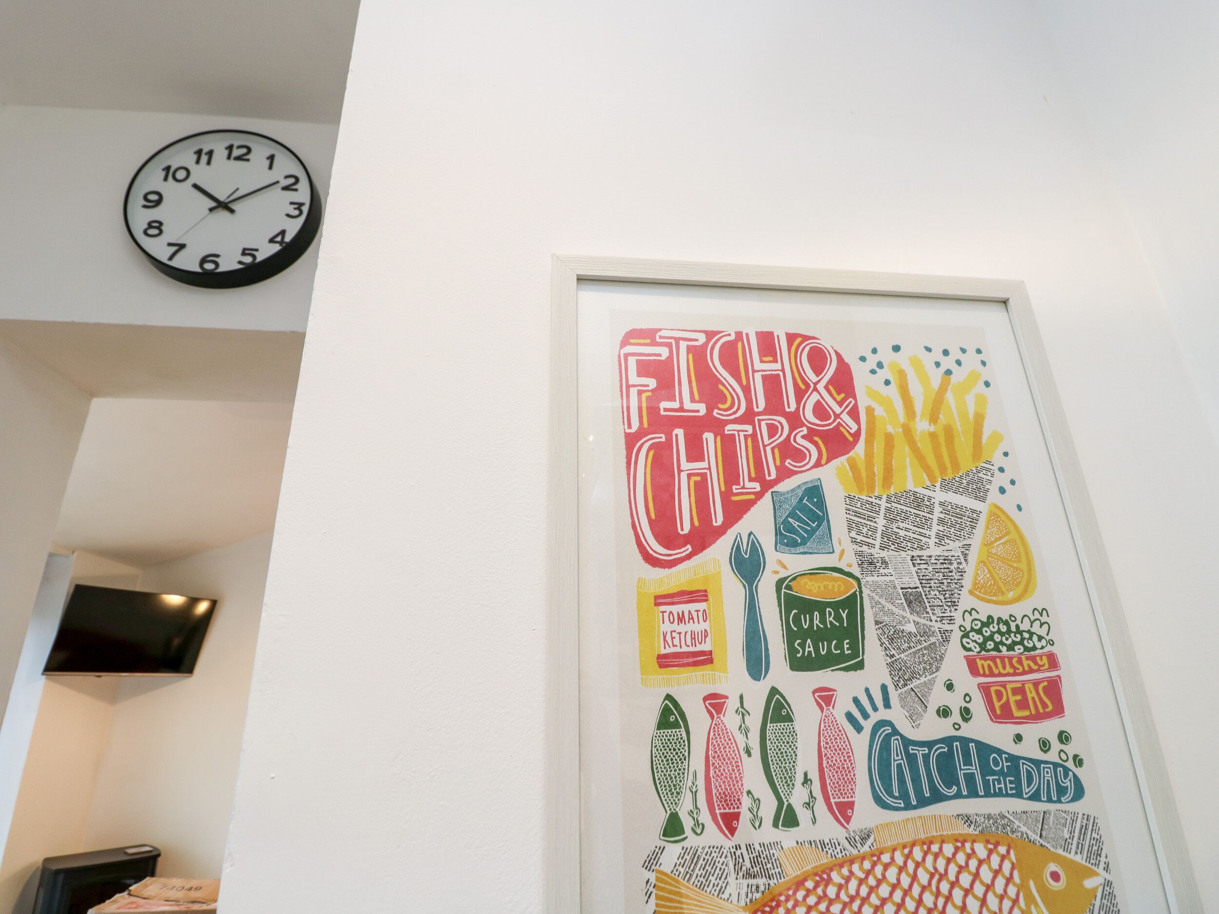 Un mur orné d’une œuvre d’art encadrée intitulée « FISH & CHIPS », représentant divers aliments et ustensiles de cuisine.