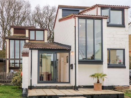 A modern two-story house with a tiled roof, large windows, and a small front garden with a potted plant.