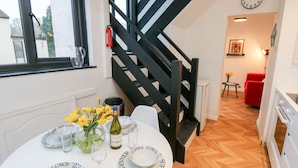 A dining area with a round table set for breakfast, lunch, and dinner. A staircase with black railings leads to another room. - Creek Lodge (Ryde)
