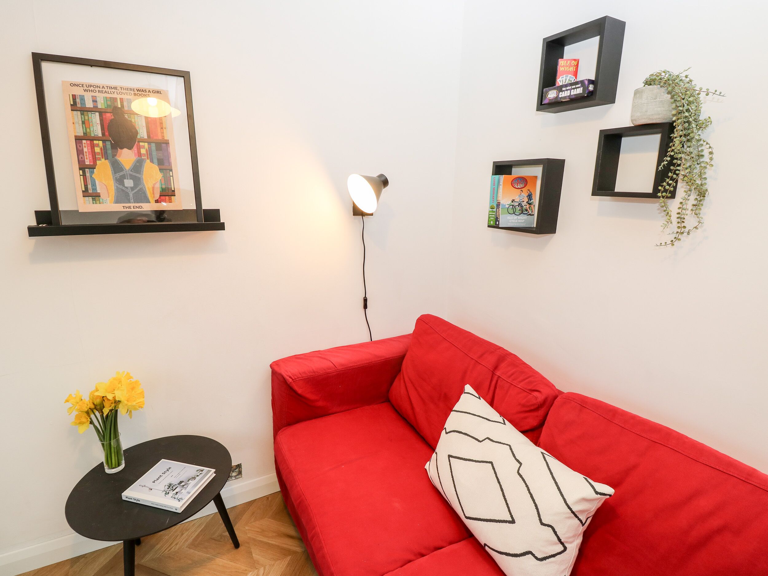A living room with a red sofa, a small black table with a vase of flowers, and a framed picture on the wall.