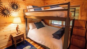 A bunk bed with a nightstand and lamp, wooden walls, and a window with blinds. - Honey Goat Hill, Sleeps 10, Centrally Located with Wooded Views (Logan)