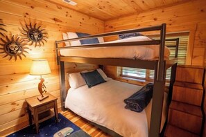 A bunk bed with a nightstand and lamp, wooden walls, and a window with blinds. - Honey Goat Hill, Sleeps 10, Centrally Located with Wooded Views (Logan)