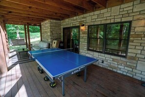 A ping pong table in a covered outdoor area with a stone wall and windows. - Honey Goat Hill, Sleeps 10, Centrally Located with Wooded Views (Logan)