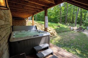 A hot tub under a wooden pergola with a stone wall, surrounded by a wooded area. - Honey Goat Hill, Sleeps 10, Centrally Located with Wooded Views (Logan)