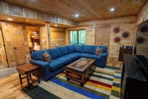 Un interior de madera con un sofá seccional azul, una mesita y una alfombra colorida a rayas.