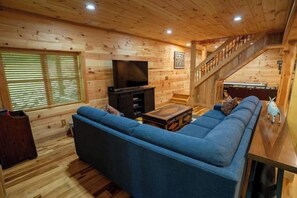 Un interior de madera con sofá, televisor y escalera.