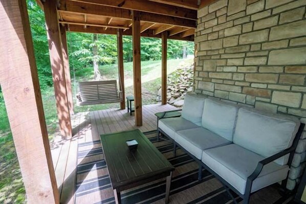 A covered outdoor seating area with a stone wall, a wooden table, and a sofa.