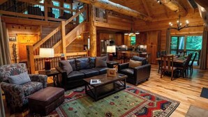 A spacious log cabin interior with a large living area, a dining area, and a staircase leading to an upper level. - Honey Goat Hill, Sleeps 10, Centrally Located with Wooded Views (Logan)