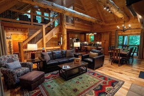 A spacious log cabin interior with a large living area, a dining area, and a staircase leading to an upper level. - Honey Goat Hill, Sleeps 10, Centrally Located with Wooded Views (Logan)