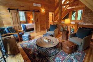 A cozy cabin interior with a bed, two sofas, a coffee table, and a fireplace.