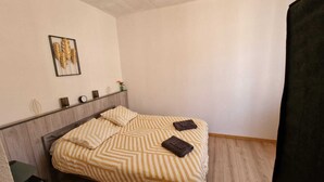 A bedroom with a bed, a headboard, a framed artwork on the wall, and a small table with a vase and a candle.