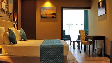 A hotel room with a large bed, a desk, and a chair. There is a painting on the wall and a view of the outside through a window.