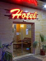 Entrada de un hotel con un letrero de neón, una recepción y una zona de estar en el interior.