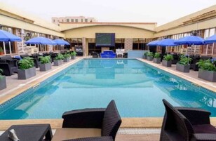 Una piscina con sillas de descanso y sombrillas, rodeada por un edificio con techo plano y amplias ventanas.