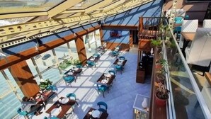 A spacious outdoor dining area with multiple tables and chairs, a wooden deck, and potted plants. - LB Suites Hotel (Bir El Djir)
