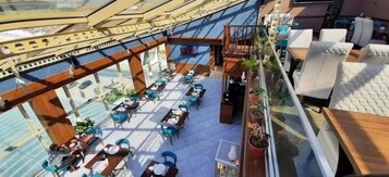 Un amplio espacio exterior con mesas y sillas, una terraza de madera y plantas en macetas.