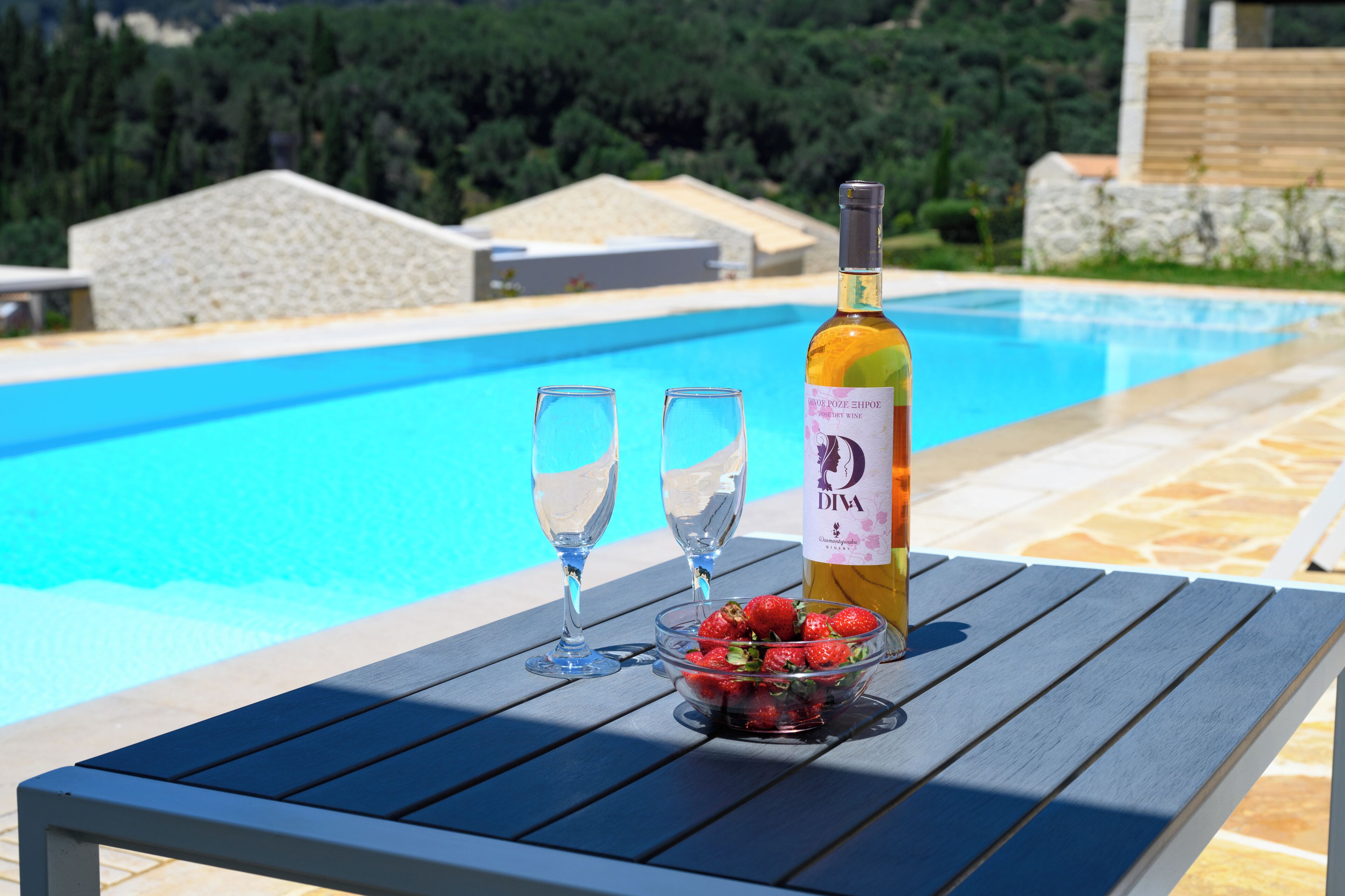 A poolside table with a bottle of wine, two glasses, and a bowl of strawberries.