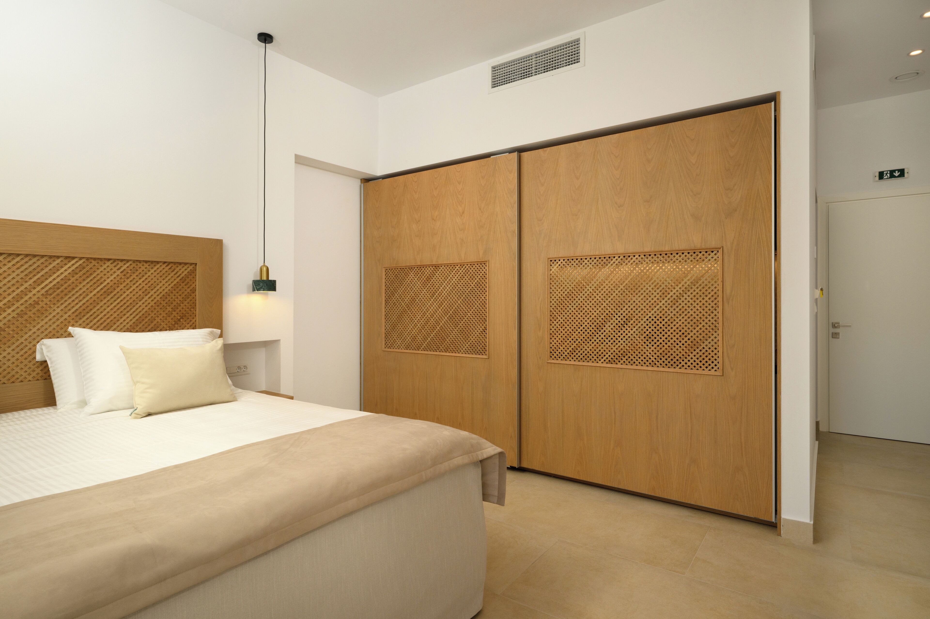 Hotelkamer met een bed, nachtkastje, lamp en een garderobe met een houten afwerking en geperforeerde panelen.