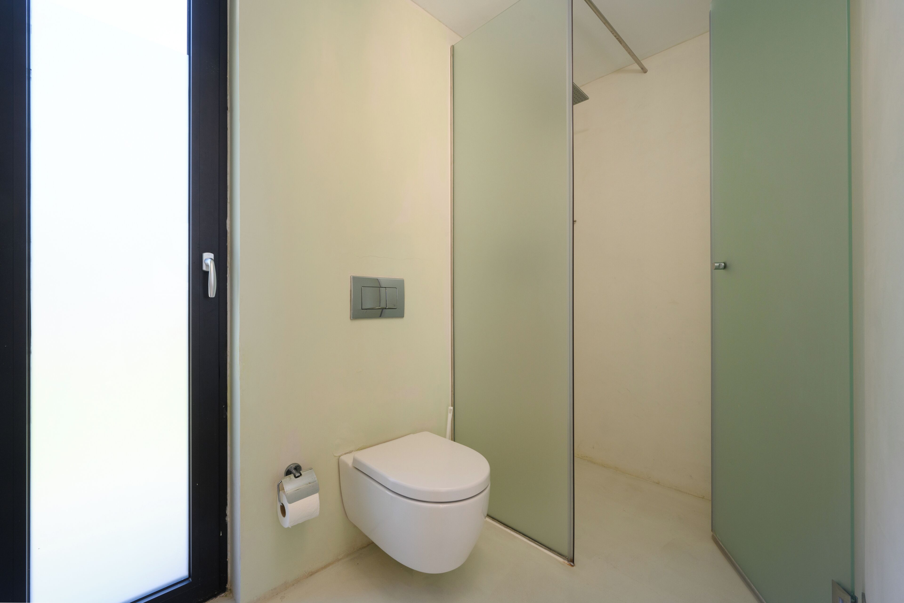 Un baño moderno con inodoro, cabina de ducha de vidrio y soporte para papel higiénico.