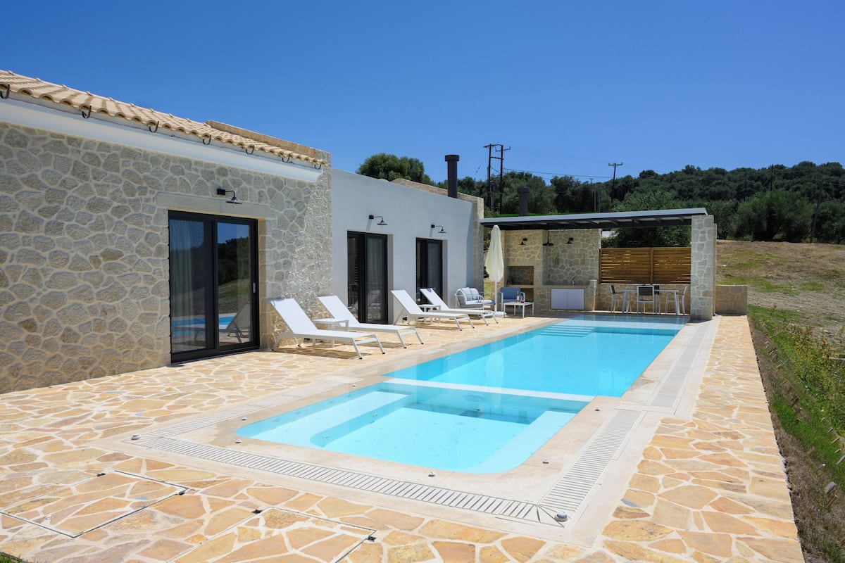 A pool area with stone flooring, lounge chairs, and a small outdoor kitchen.