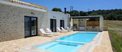 A pool area with stone flooring, lounge chairs, and a small outdoor kitchen.