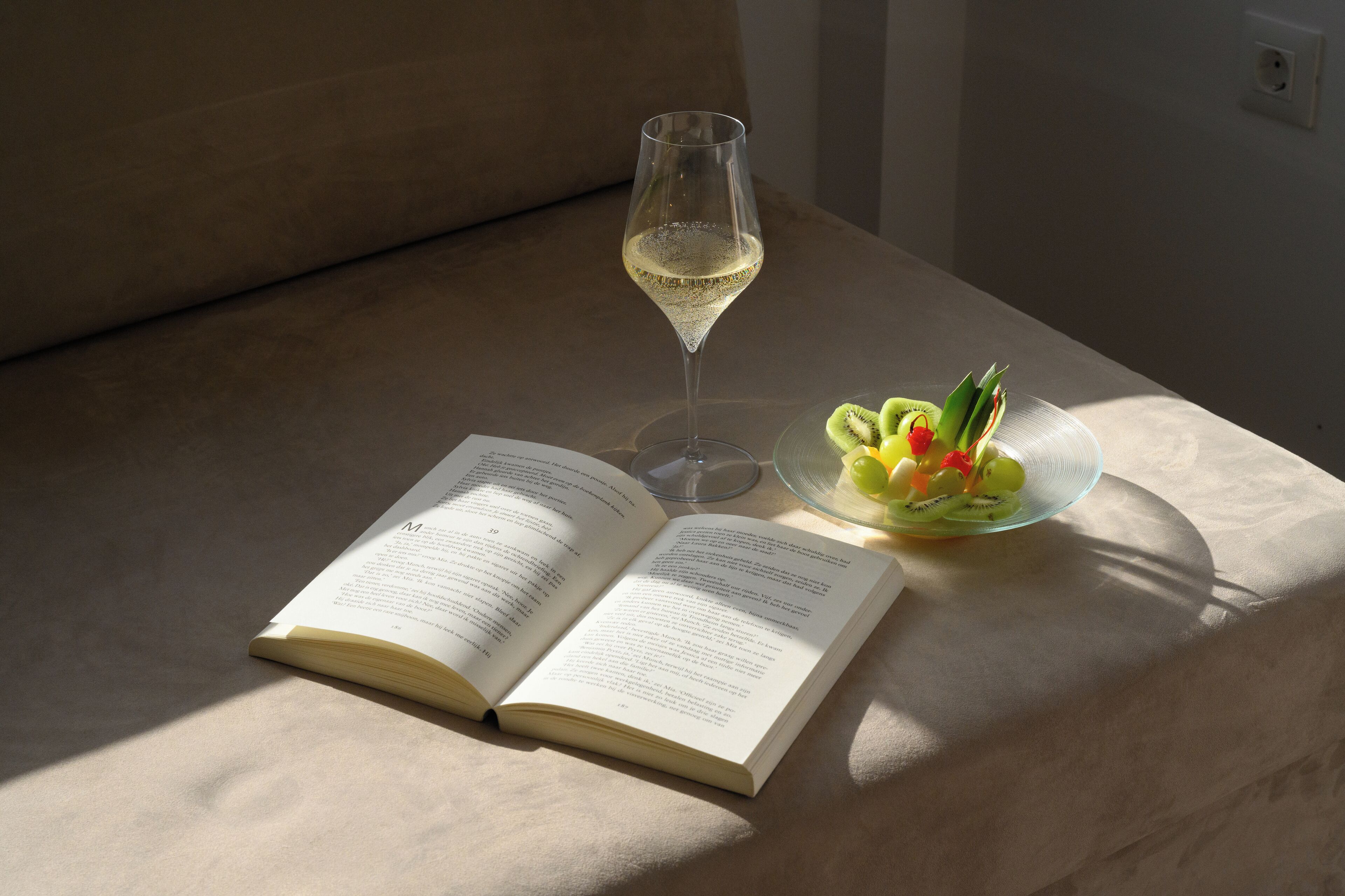 Ein offenes Buch auf einem Tisch mit einem Glas Weißwein und einer Obstplatte.