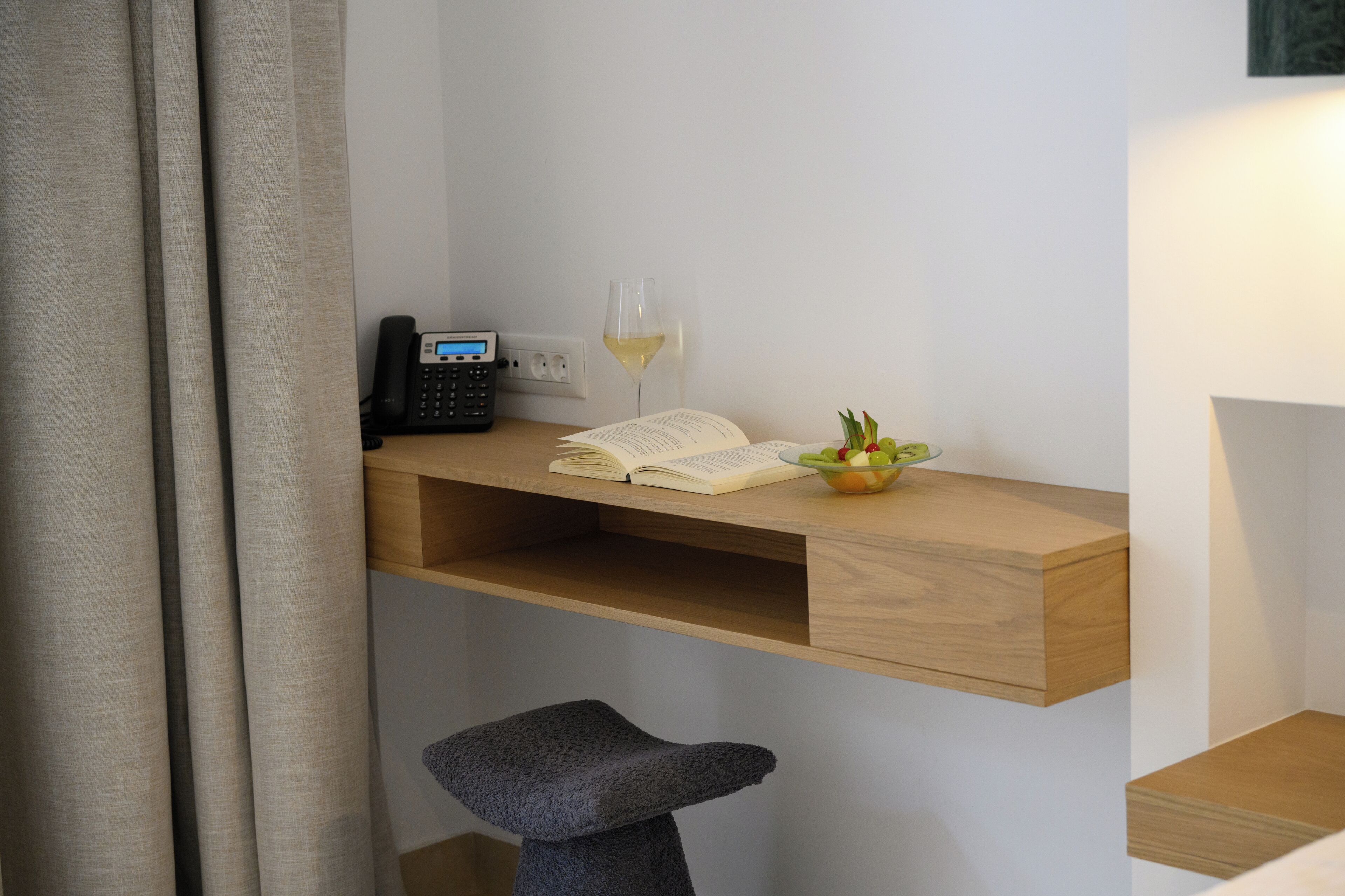 Een werkplek met een bureau, een telefoon, een open boek, een glas wijn en een kleine plant.