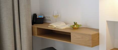 Een werkplek met een bureau, een telefoon, een open boek, een glas wijn en een kleine plant.