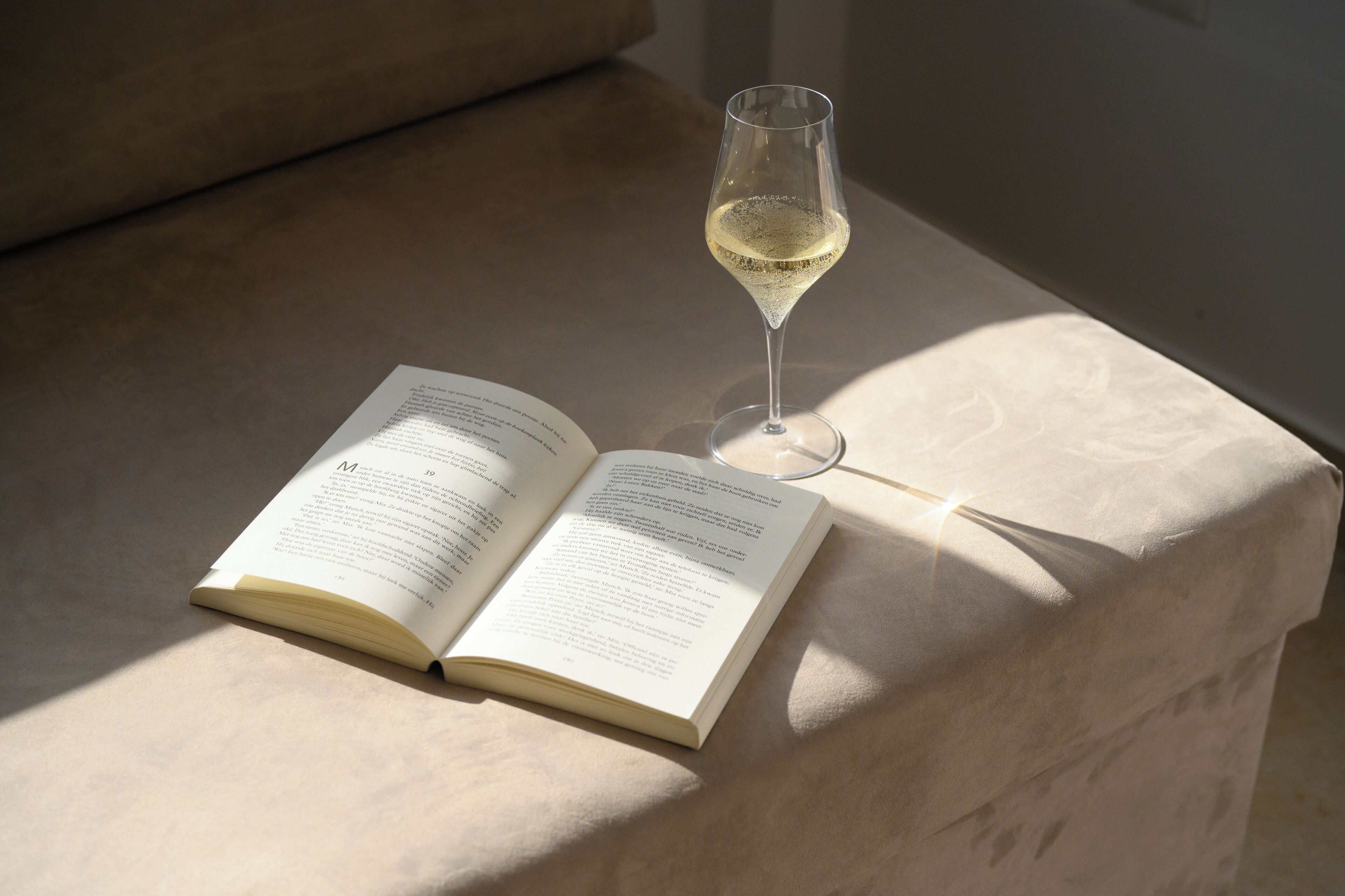 Ein offenes Buch auf einer hellen Oberfläche, daneben ein Glas Weißwein.