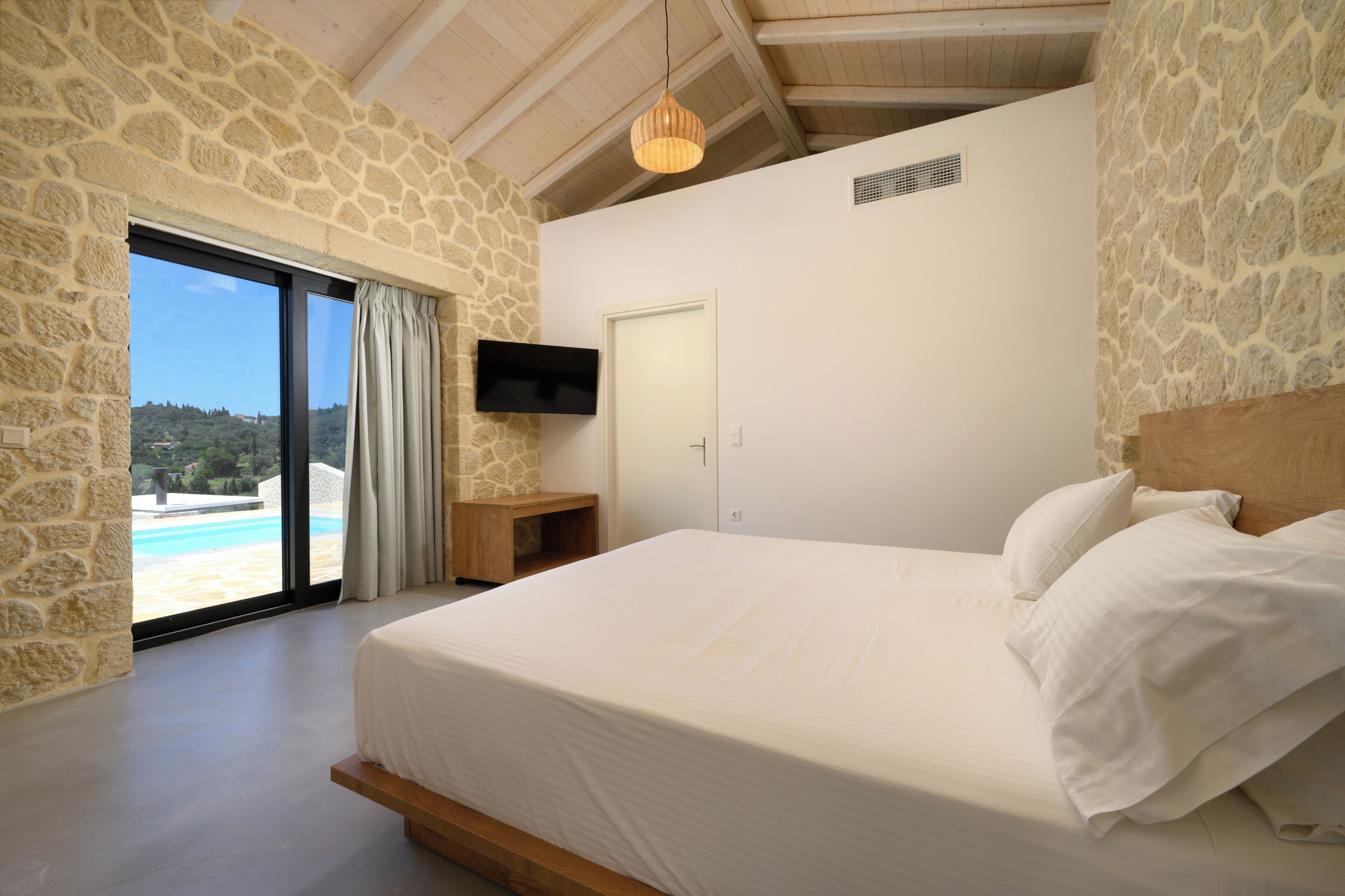 Une chambre avec des murs en pierre, un grand lit, une télévision et une vue sur une piscine.