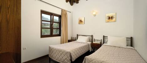 A room with two beds, wooden flooring, a window with curtains, and artwork on the walls.
