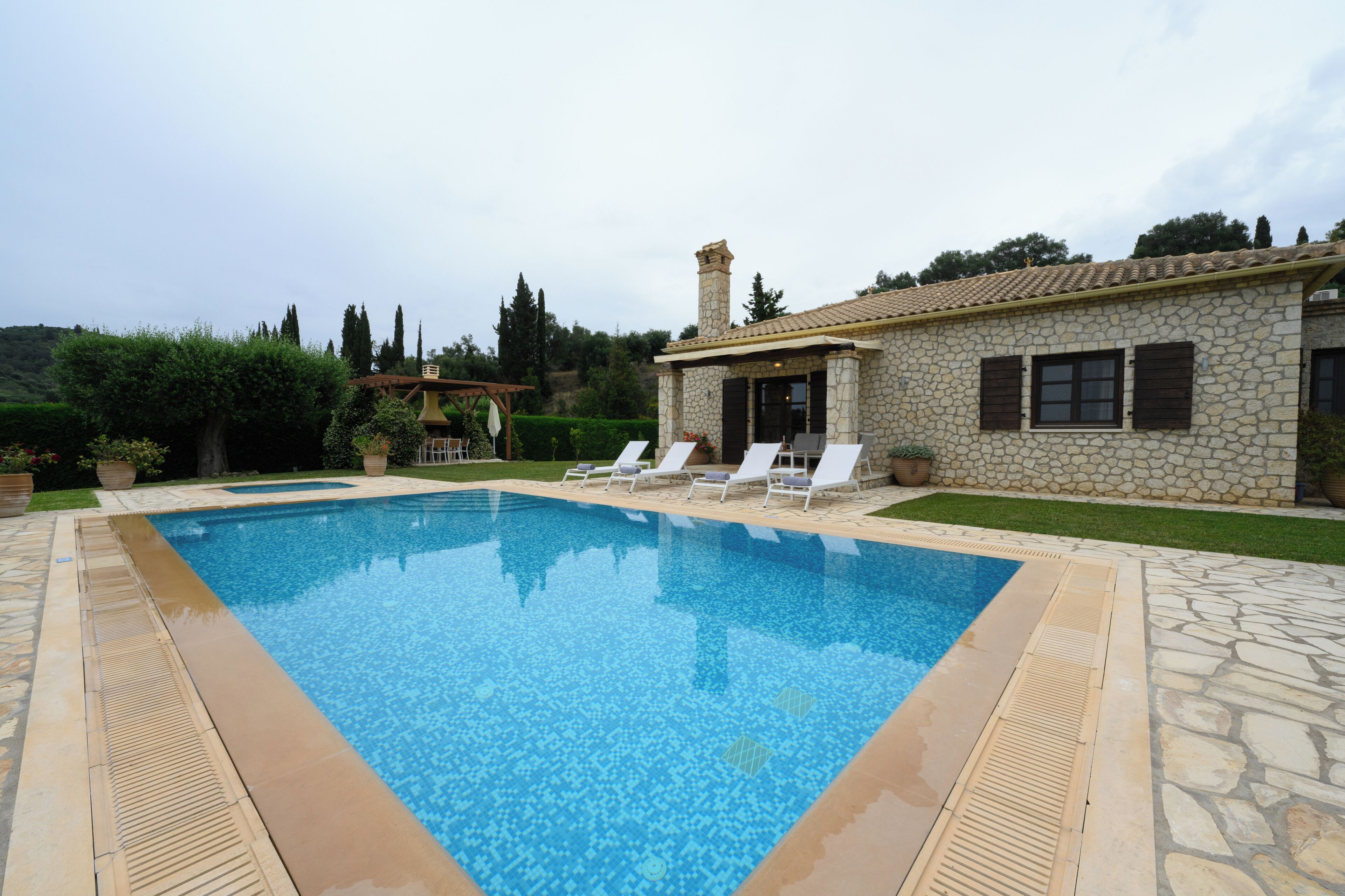 A stone building with a swimming pool, lounge chairs, and a pergola.