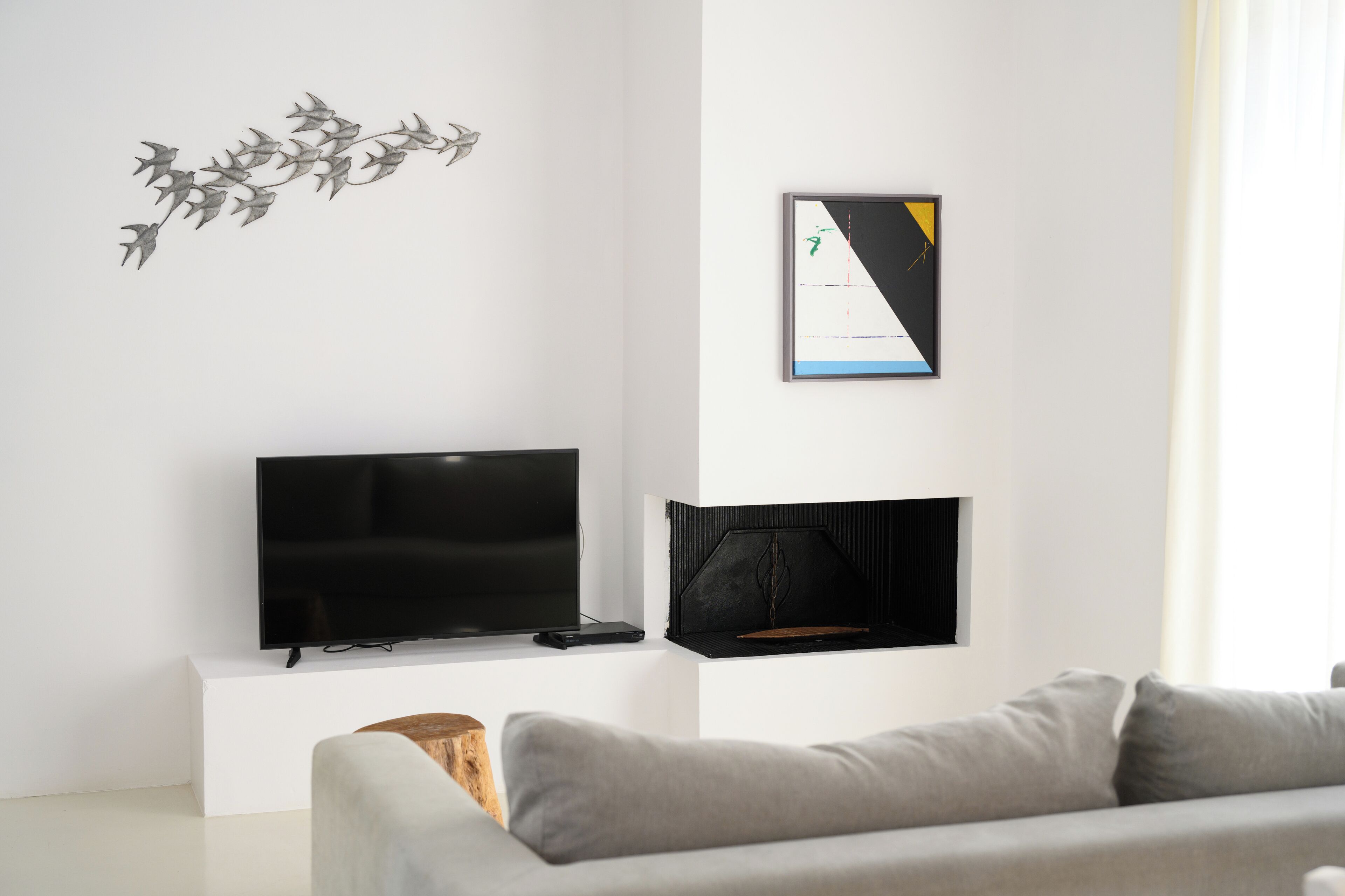 Una sala de estar moderna con un televisor de pantalla plana sobre un soporte blanco, una chimenea negra y un sofá gris.
