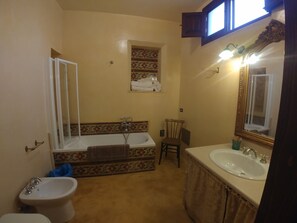 A bathroom with a bathtub, a sink, and a toilet. There is a mirror with lights above it, and a window with curtains. - MASSERIA LA MAESTA' 1511 (Sannicola)