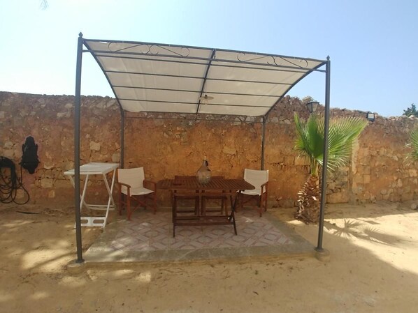 An outdoor patio with a wooden table and chairs, a white tablecloth, and a metal canopy. - MASSERIA LA MAESTA' 1511 (Sannicola)