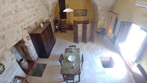 A room with a high arched stone ceiling, a wooden dining table with chairs, a small cabinet, and a cross on the wall. - MASSERIA LA MAESTA' 1511 (Sannicola)
