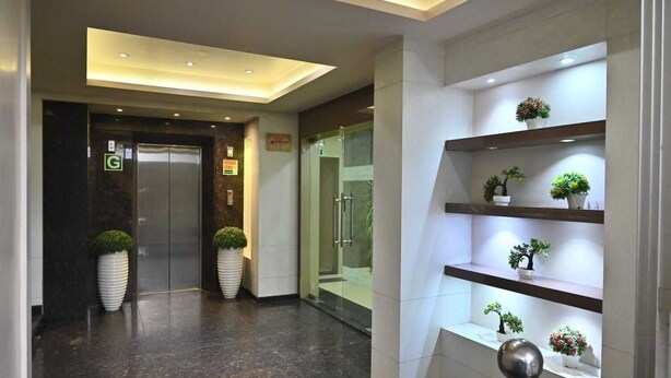 A modern hotel lobby with a reception desk, a glass elevator, and potted plants on shelves. - HOTEL ROYAL COTTAGE (Kanpur)