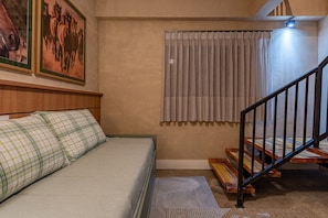A bedroom with a bed, a wooden headboard, a window with curtains, a staircase, and a wall-mounted light. - Fazenda Realeza (Pedra Bela)
